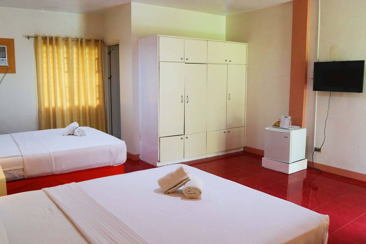 A hotel room with two beds, a wardrobe, a television, and a small refrigerator.