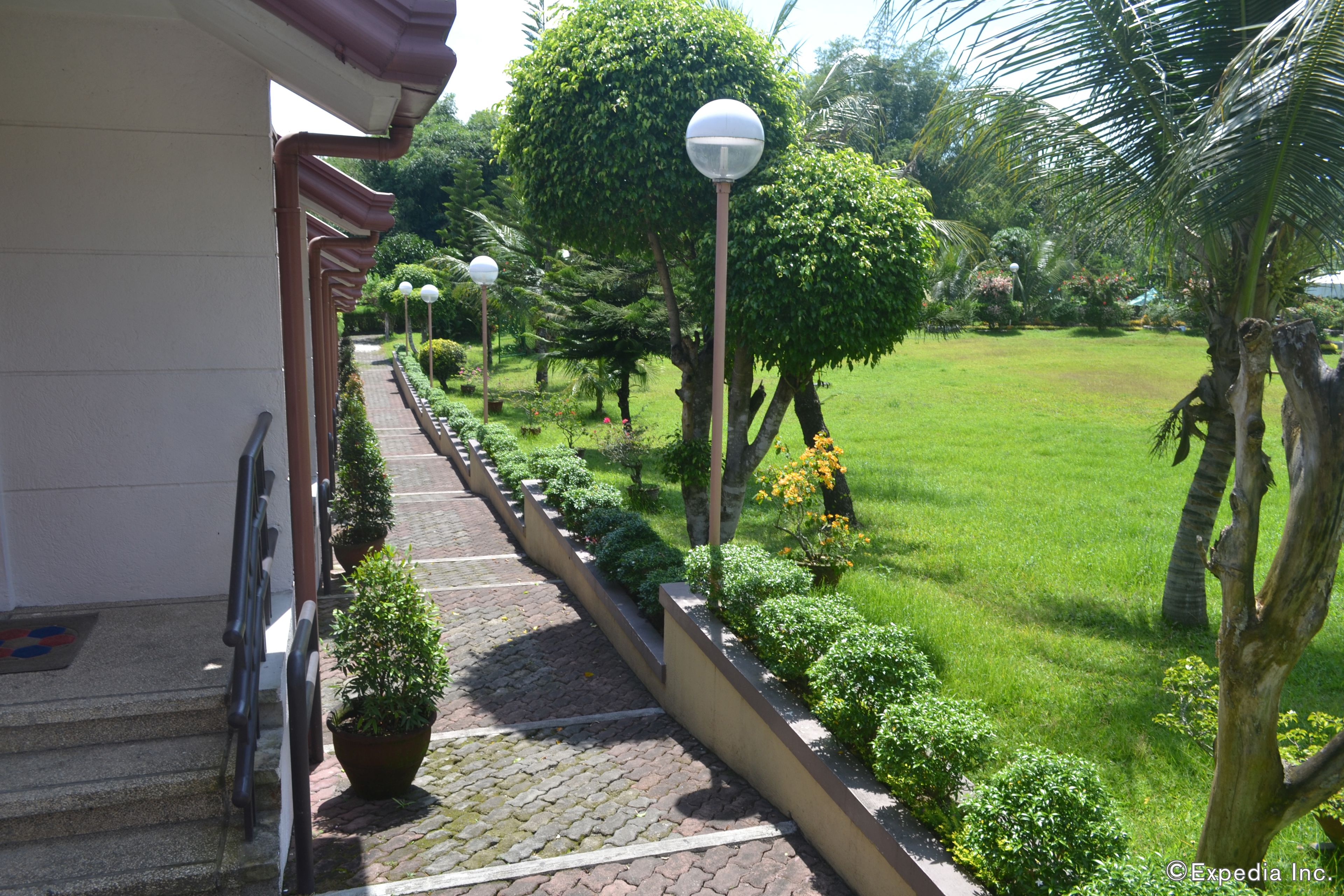 A pathway leading to a building with a covered entrance, surrounded by well-maintained greenery and palm trees.