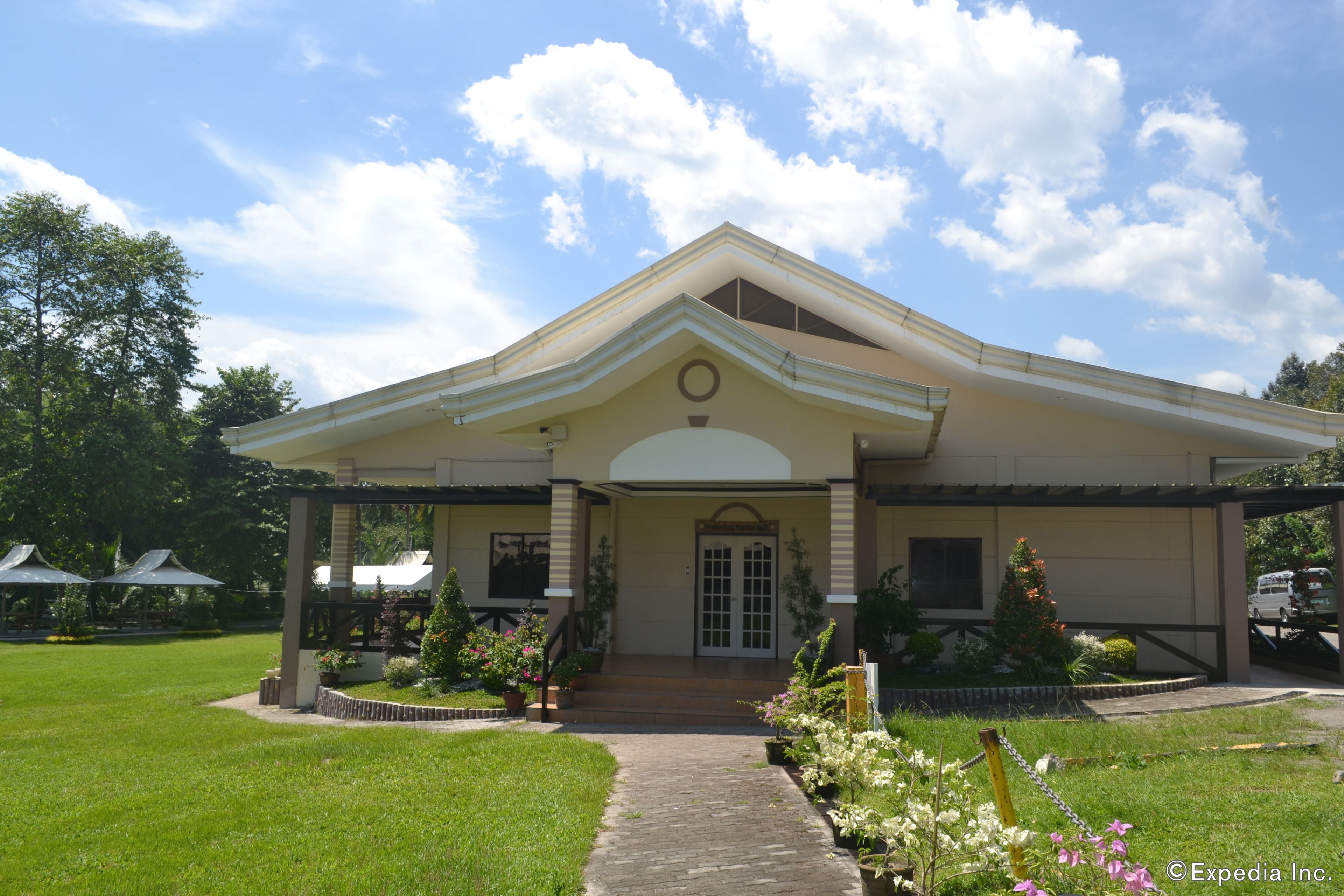 A two-story building with a central entrance, a covered porch, and a garden with flowers and plants.