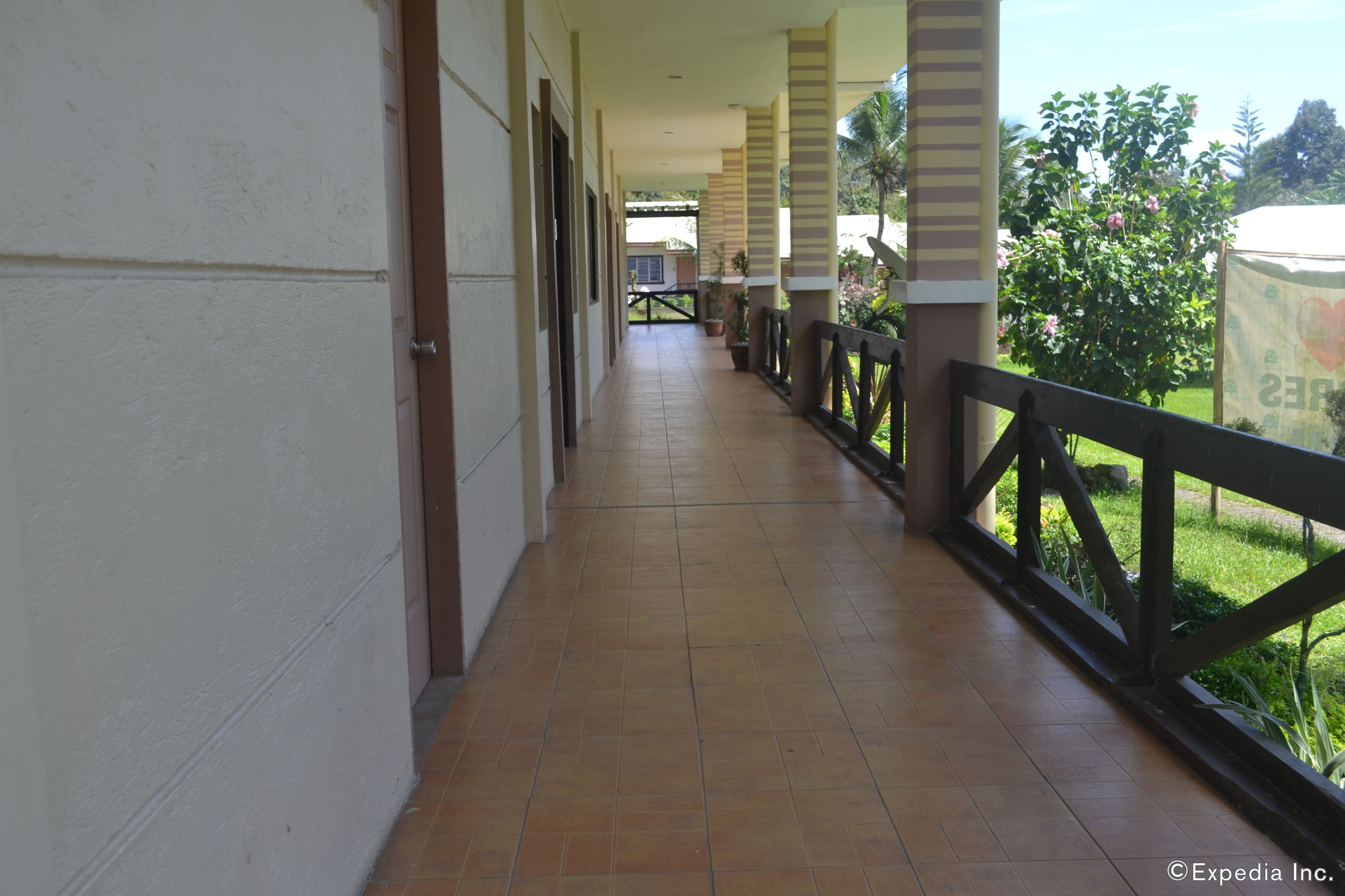A corridor with tiled flooring, white walls, and a wooden railing.