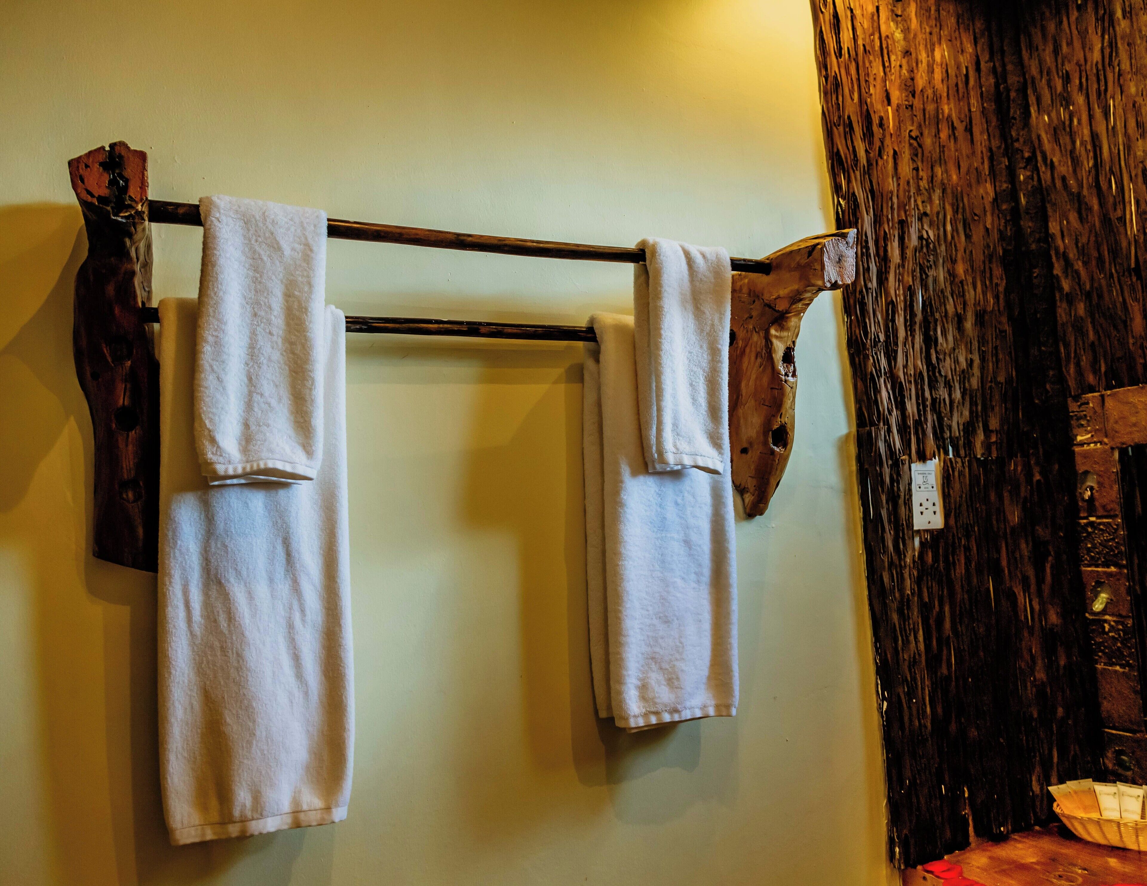 A wooden towel rack with three white towels hanging.
