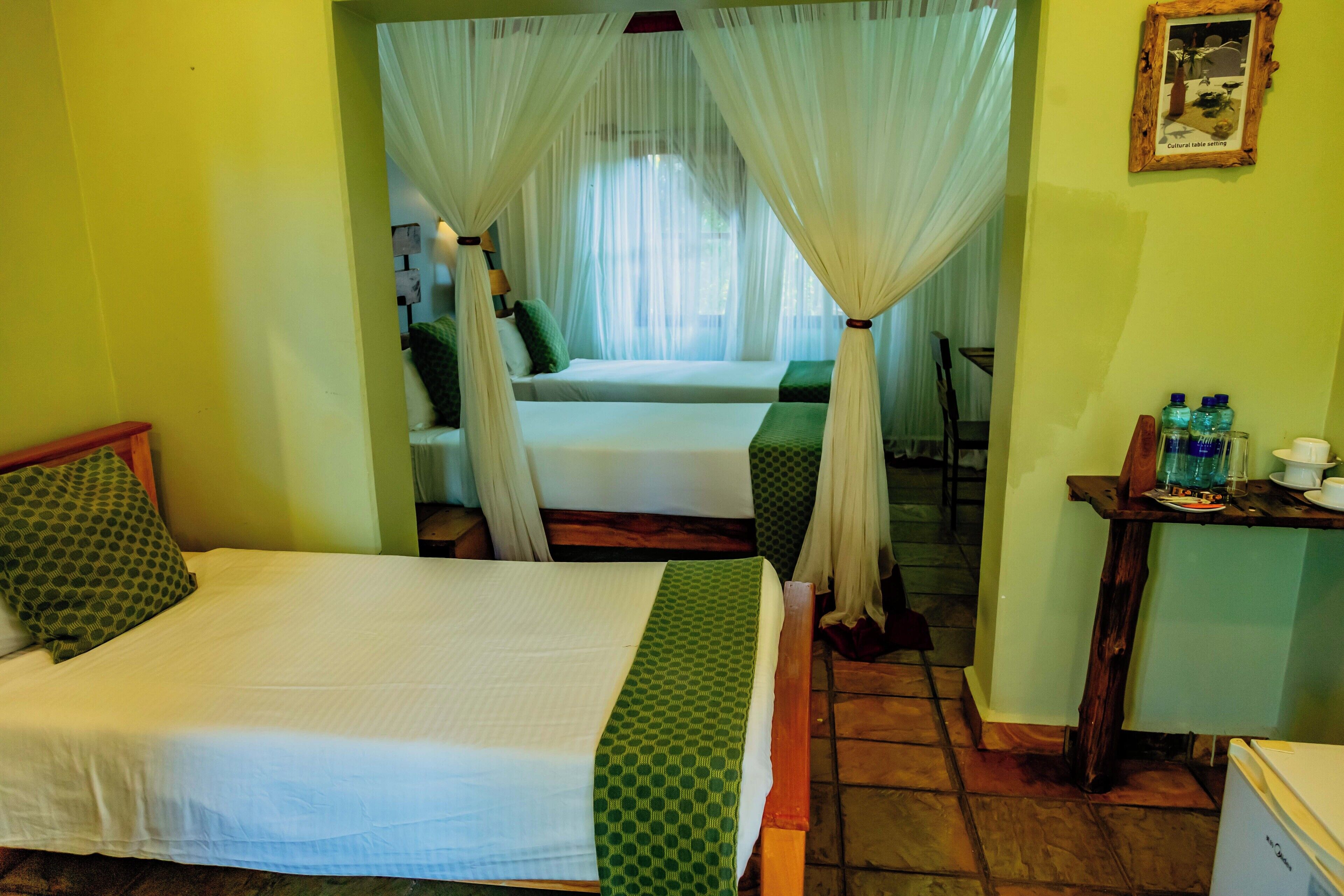 A room with two beds, a small table with bottles, and a picture on the wall.