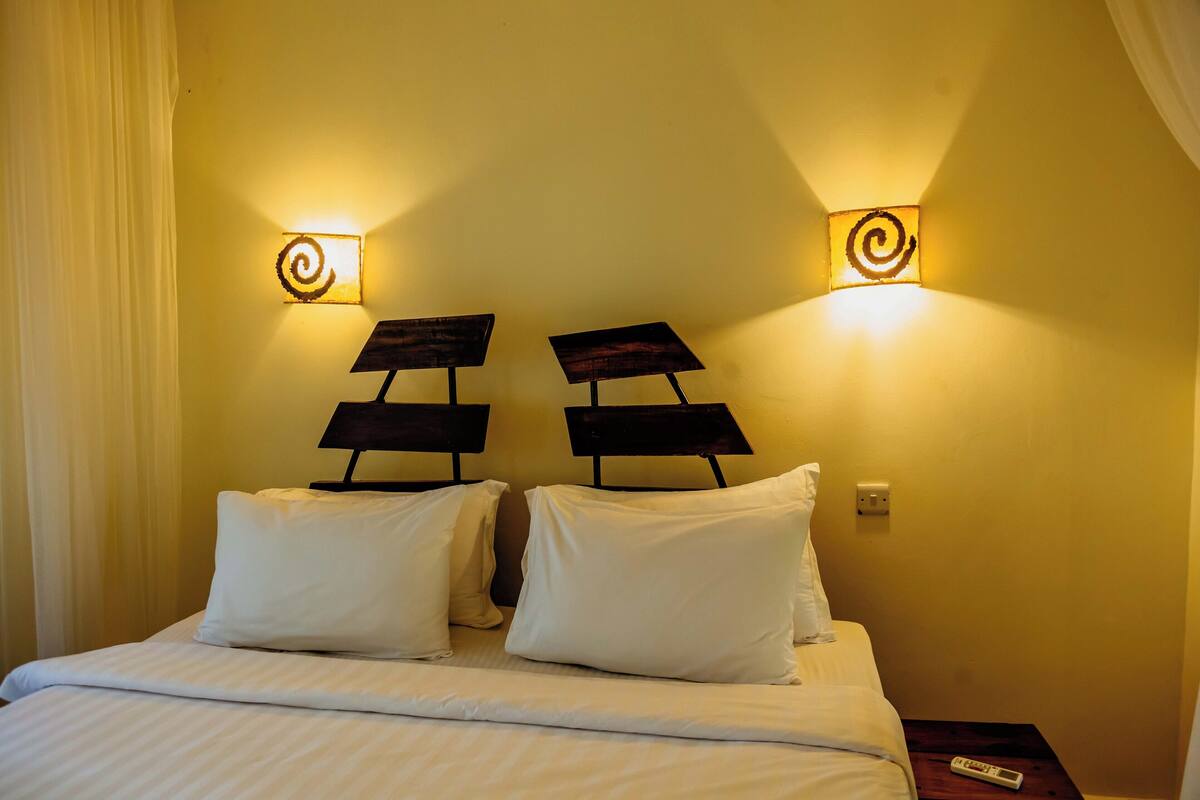 A hotel room with a bed, two wall-mounted lamps, and a nightstand with a remote control.