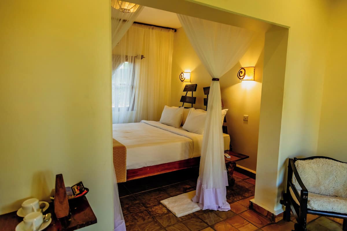 A bedroom with a bed, bedside table, chair, and a nightstand with a lamp.