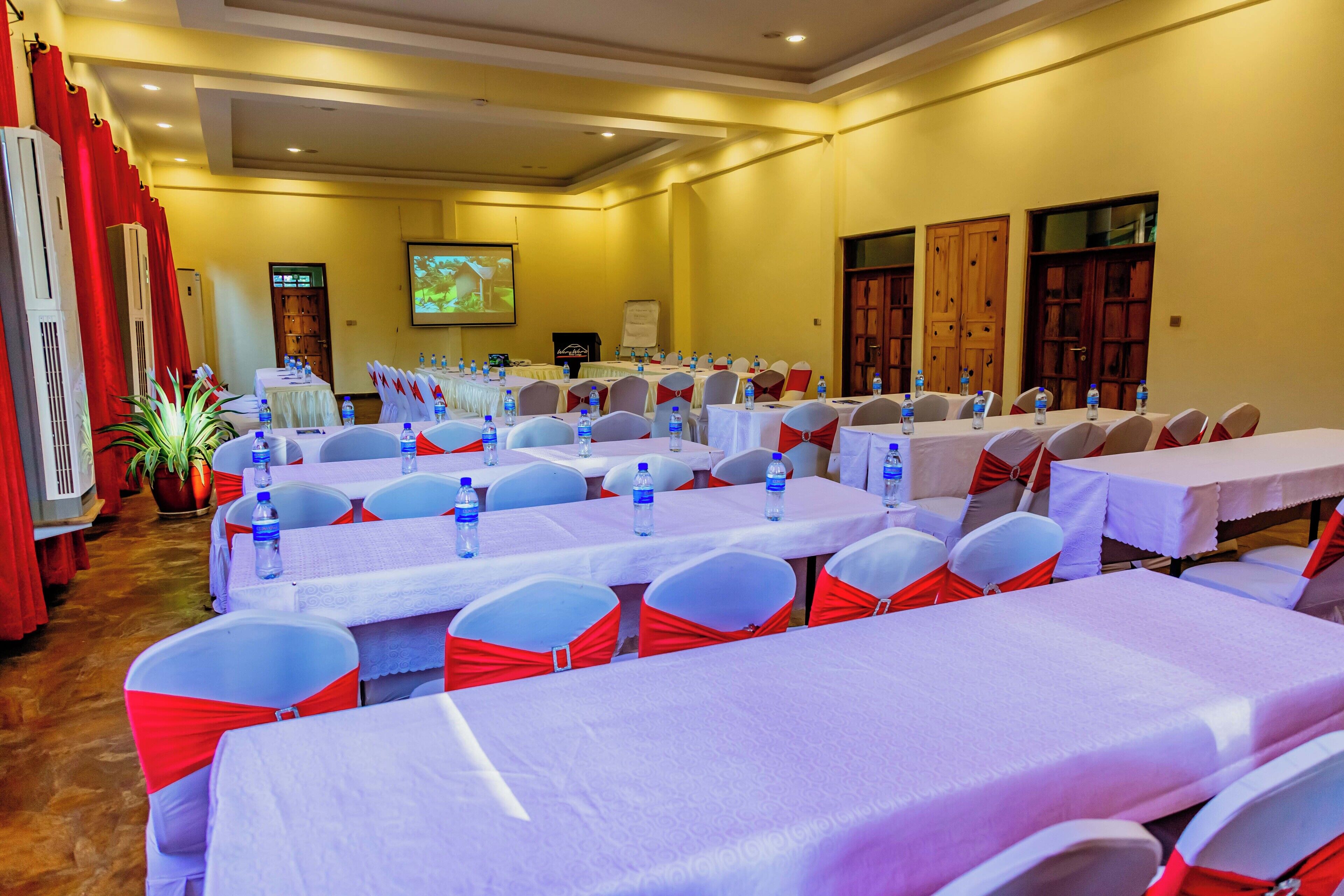 A conference room with multiple tables, chairs, and a projector screen.