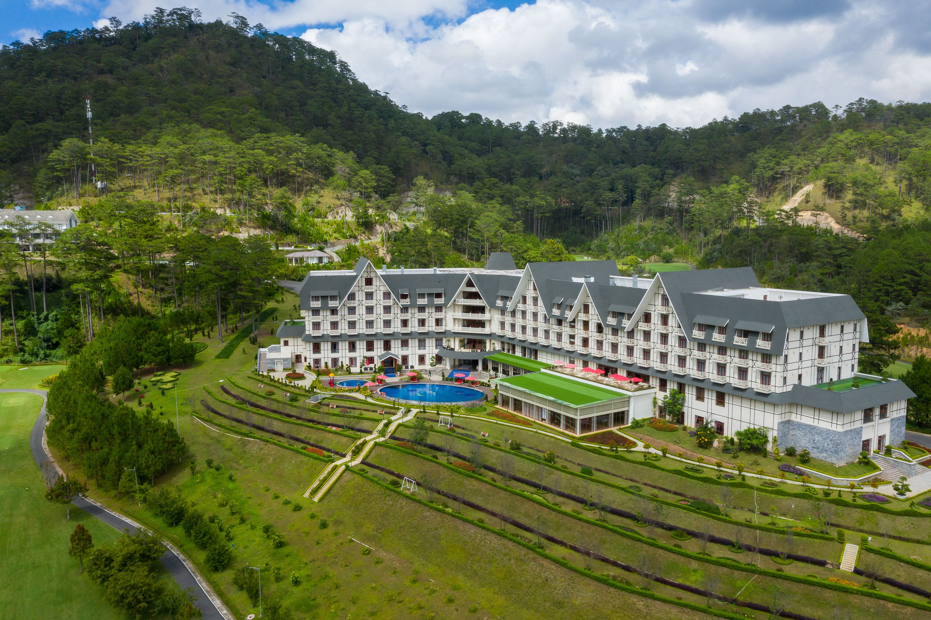 A large hotel with multiple buildings, a swimming pool, and landscaped gardens.