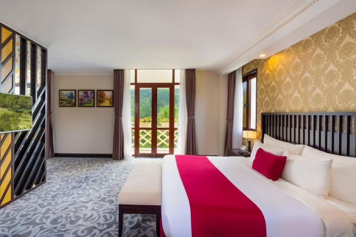 Habitación de hotel con cama, escritorio, ventana y vistas a la vegetación.
