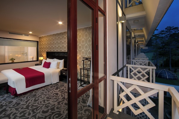 A hotel room with a large bed, a balcony with a railing, and a view of the outdoors.