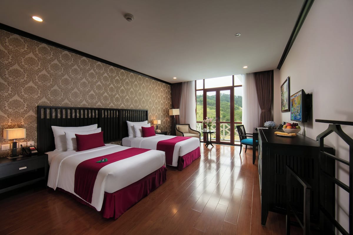 A hotel room with two beds, a desk, a chair, and a balcony with a view.