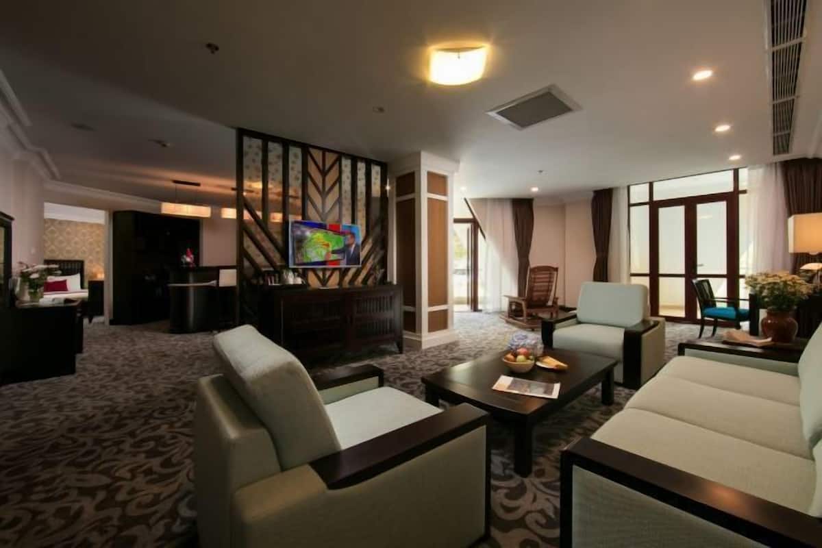 A hotel room with a sofa, armchairs, a coffee table, a TV, and a large window.