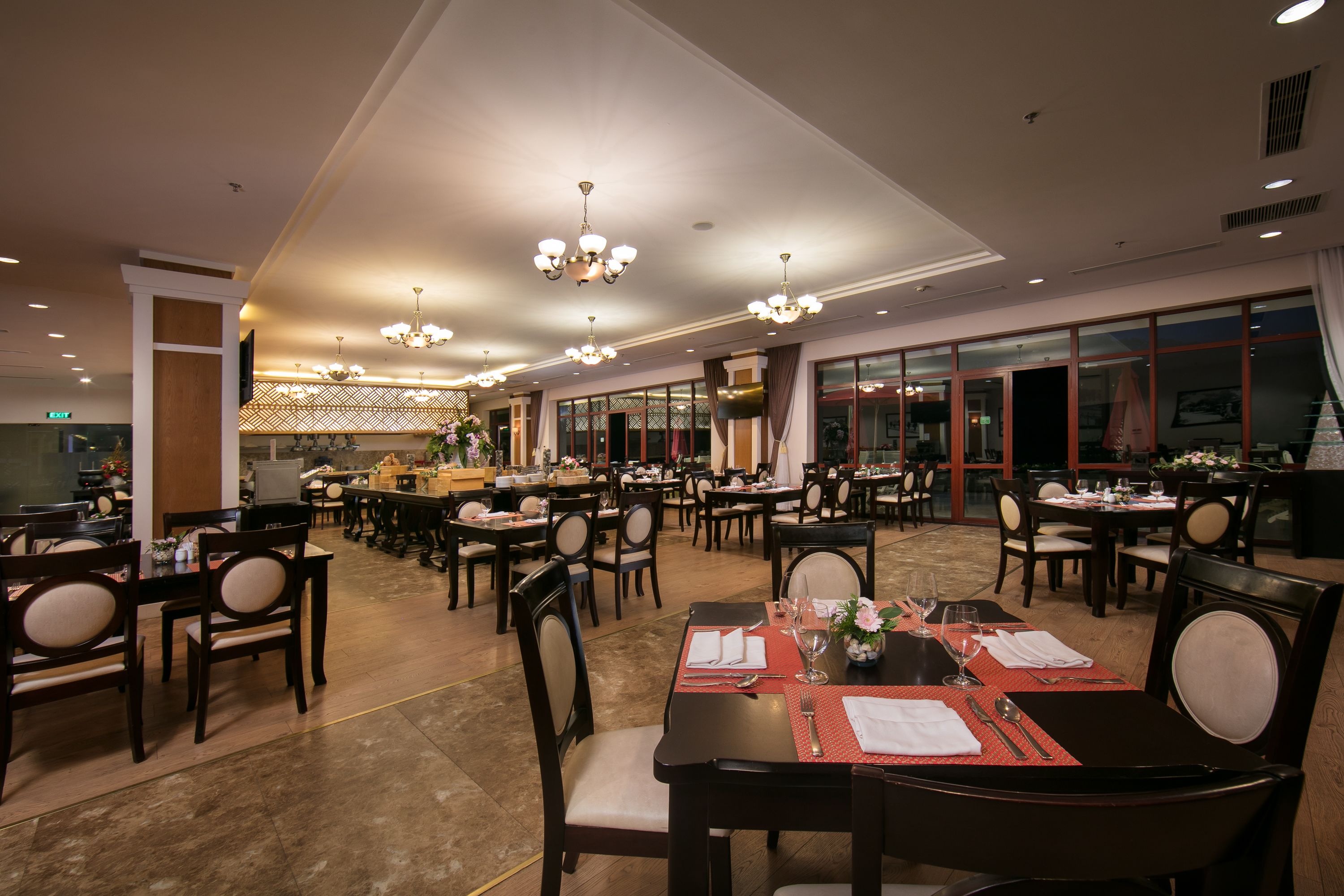 A spacious restaurant with multiple dining tables and chairs, large windows, and modern chandeliers.