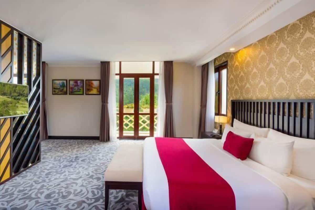 A hotel room with a bed, a desk, a window, and a view of greenery.