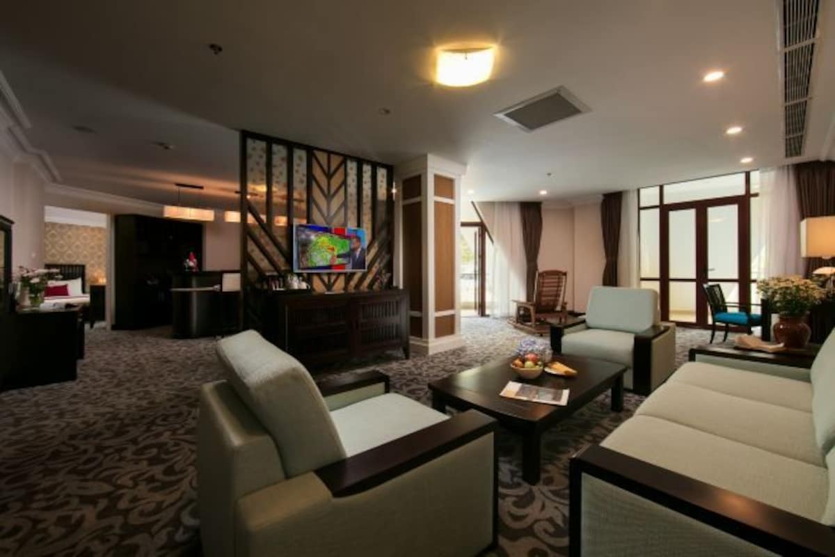 Habitación de hotel con sofá, sillones, una mesa de centro, televisión y un ventanal grande.