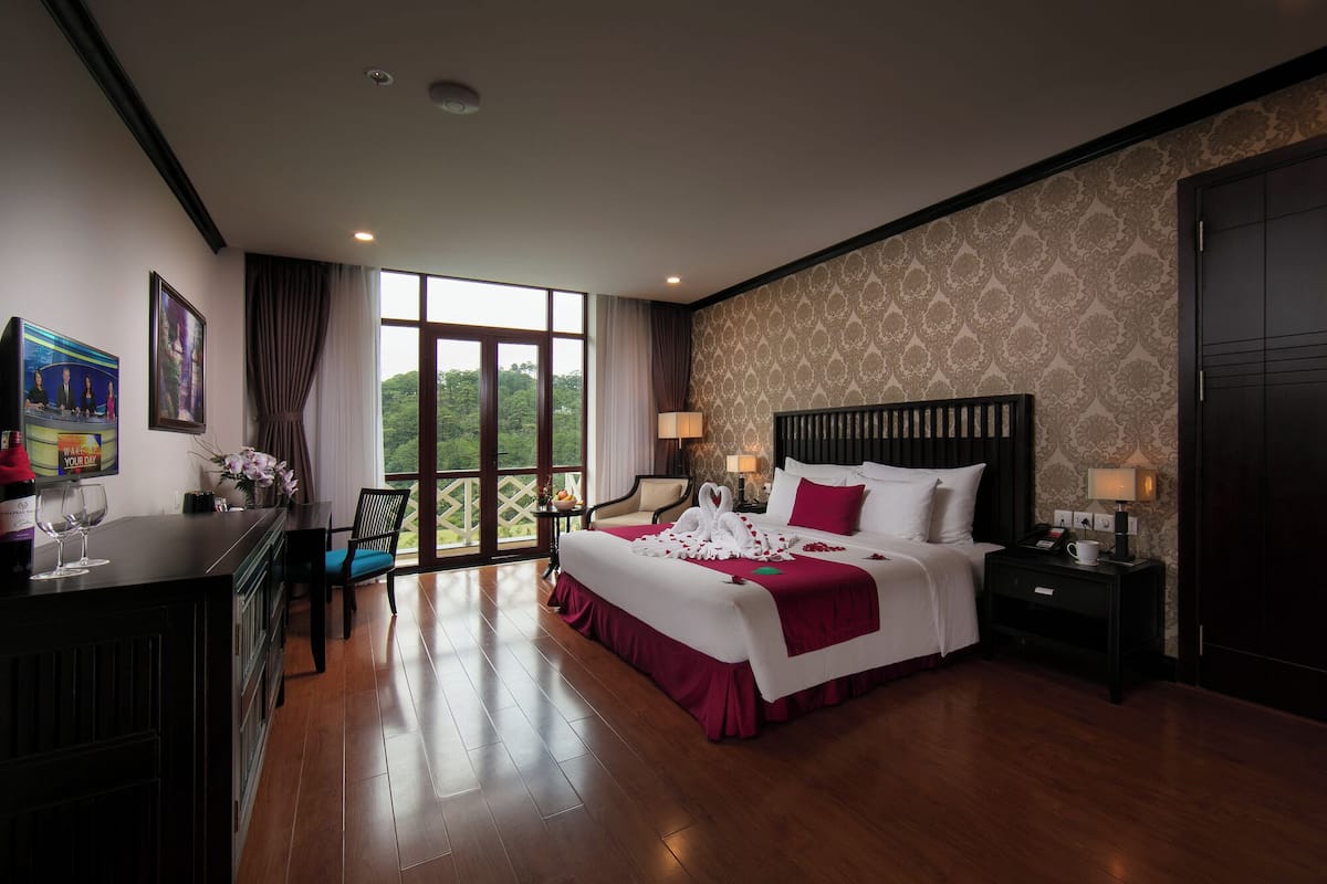 A hotel room with a large bed, a desk with a TV, a chair, and a view of the outdoors.