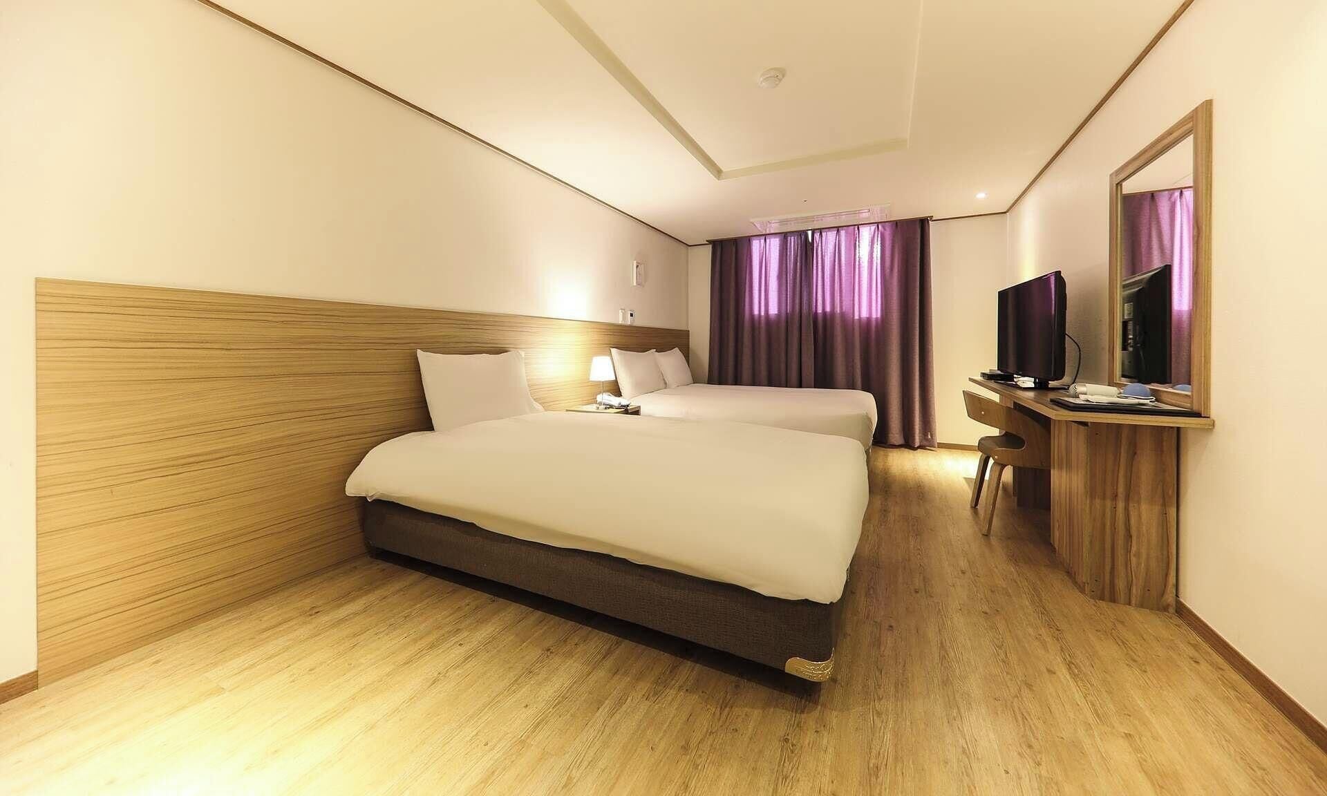A hotel room with a wooden headboard, a bed with white bedding, a desk with a computer, and a mirror.