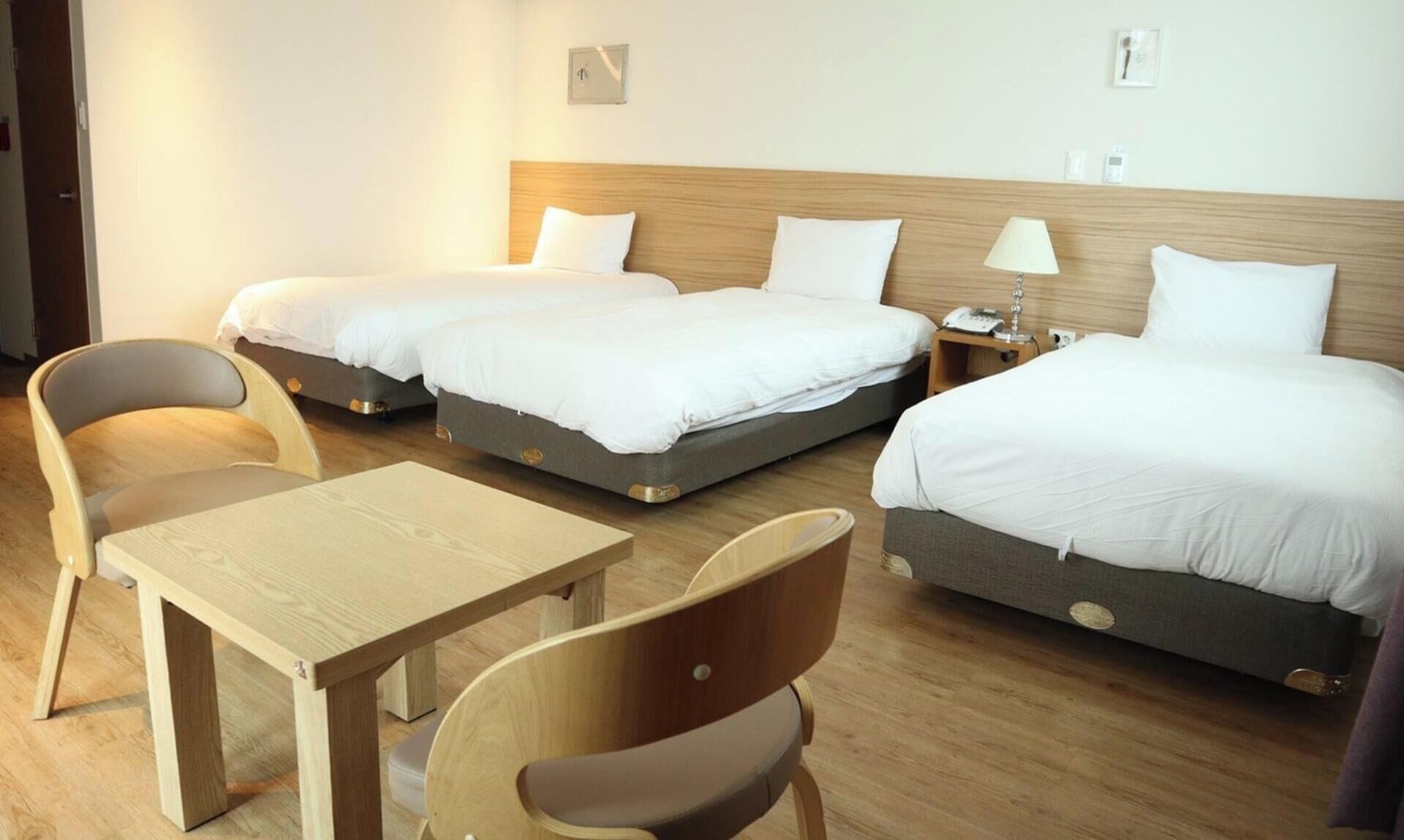 Una habitación de hotel con dos camas, una mesa de madera y dos sillas.