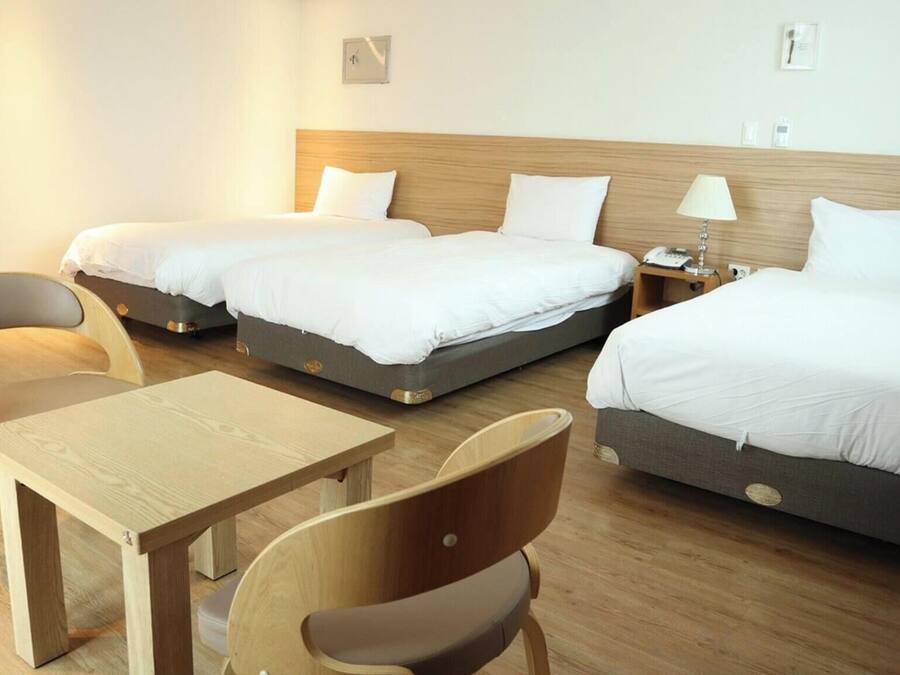 Una habitación de hotel con dos camas, una mesa de madera y dos sillas.