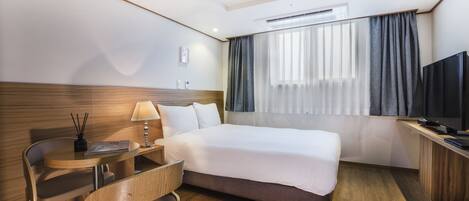 A hotel room with a bed, a desk, a chair, a TV, and a window with curtains.