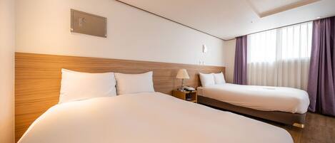 Habitación de hotel con dos camas, cabecero de madera, mesita de noche con lámpara y ventana con cortinas.