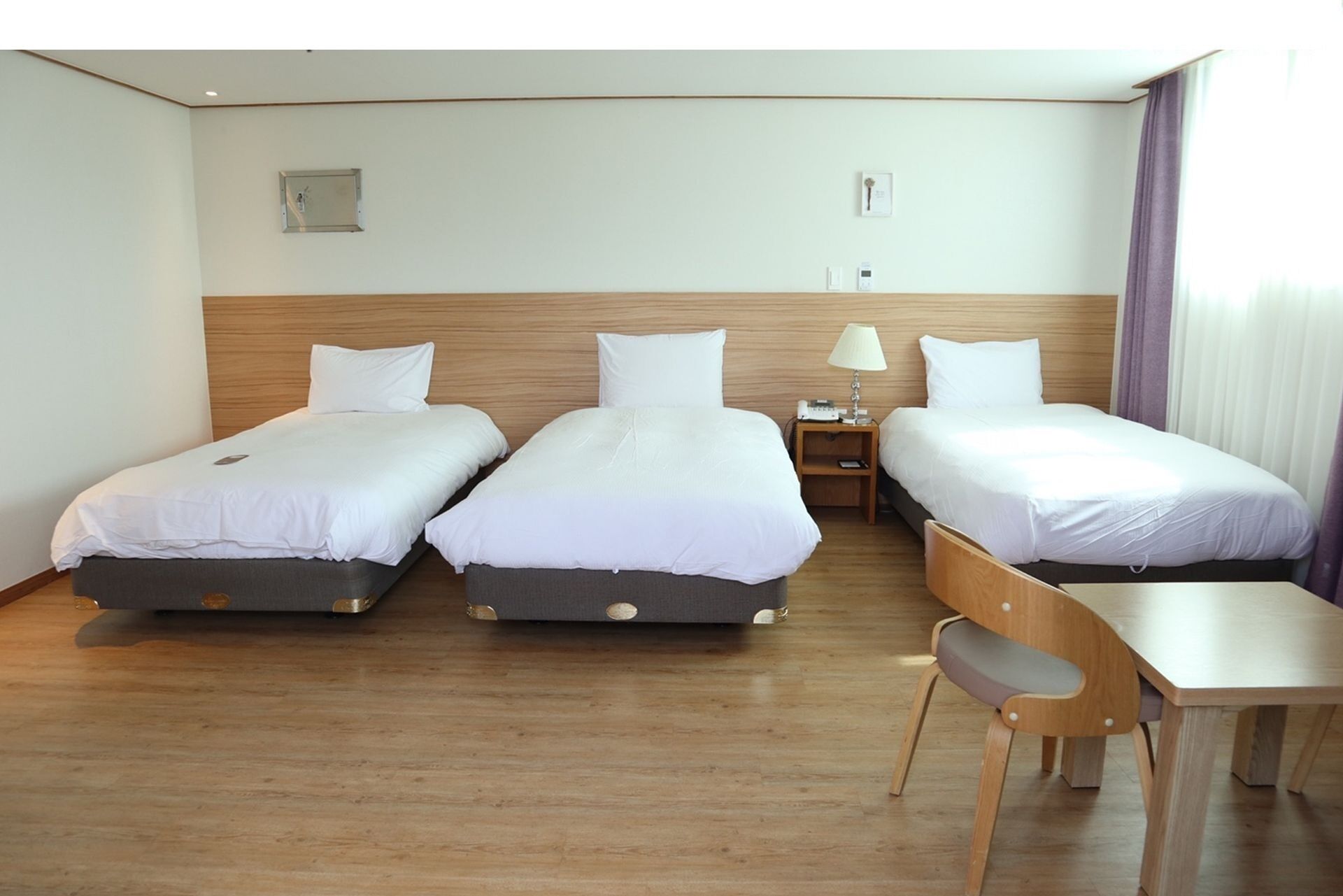 A hotel room with three single beds, a wooden desk, and a chair.