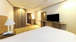 Una camera d'albergo con un letto grande, una televisione su una mensola in legno, una scrivania con una lampada e un telefono.