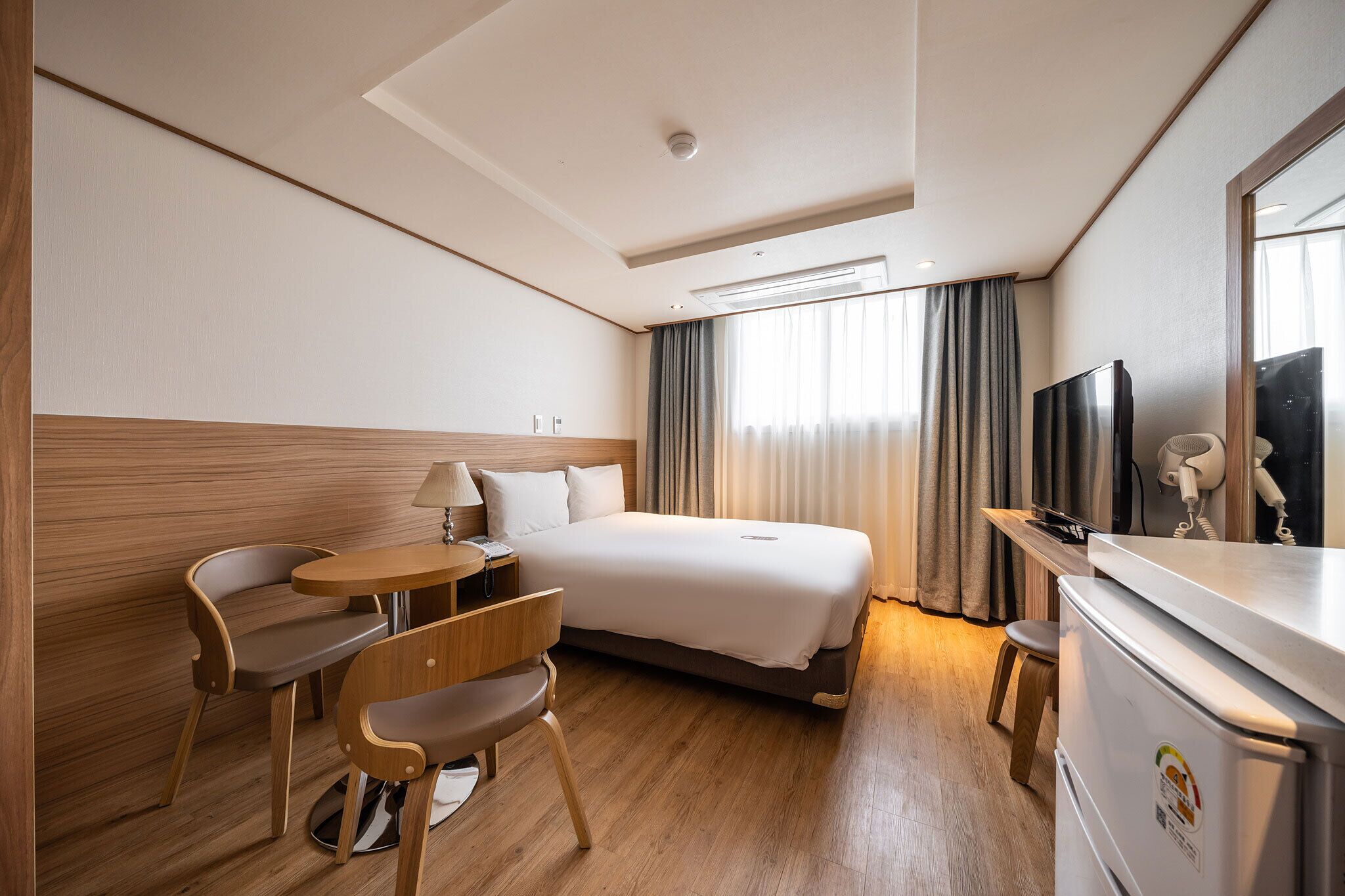 Une chambre d’hôtel comprenant un lit, un bureau, une chaise, une petite table, une lampe, un téléviseur et un réfrigérateur.