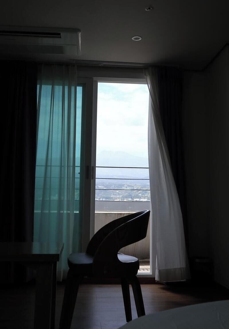 Una habitación con vistas a un paisaje urbano a través de una ventana con cortinas ligeras.