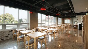 Un'ampia sala da pranzo interna con diversi tavoli e sedie, ampie finestre che offrono viste verso l'esterno, e un soffitto moderno con travi a vista e lampade pendenti rosse.