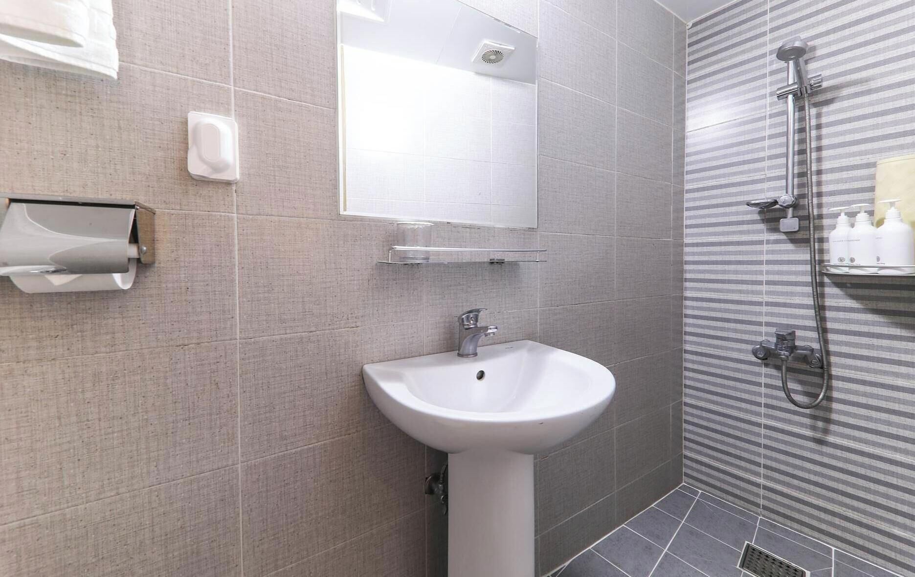 A bathroom with a sink, mirror, towel dispenser, and shower.