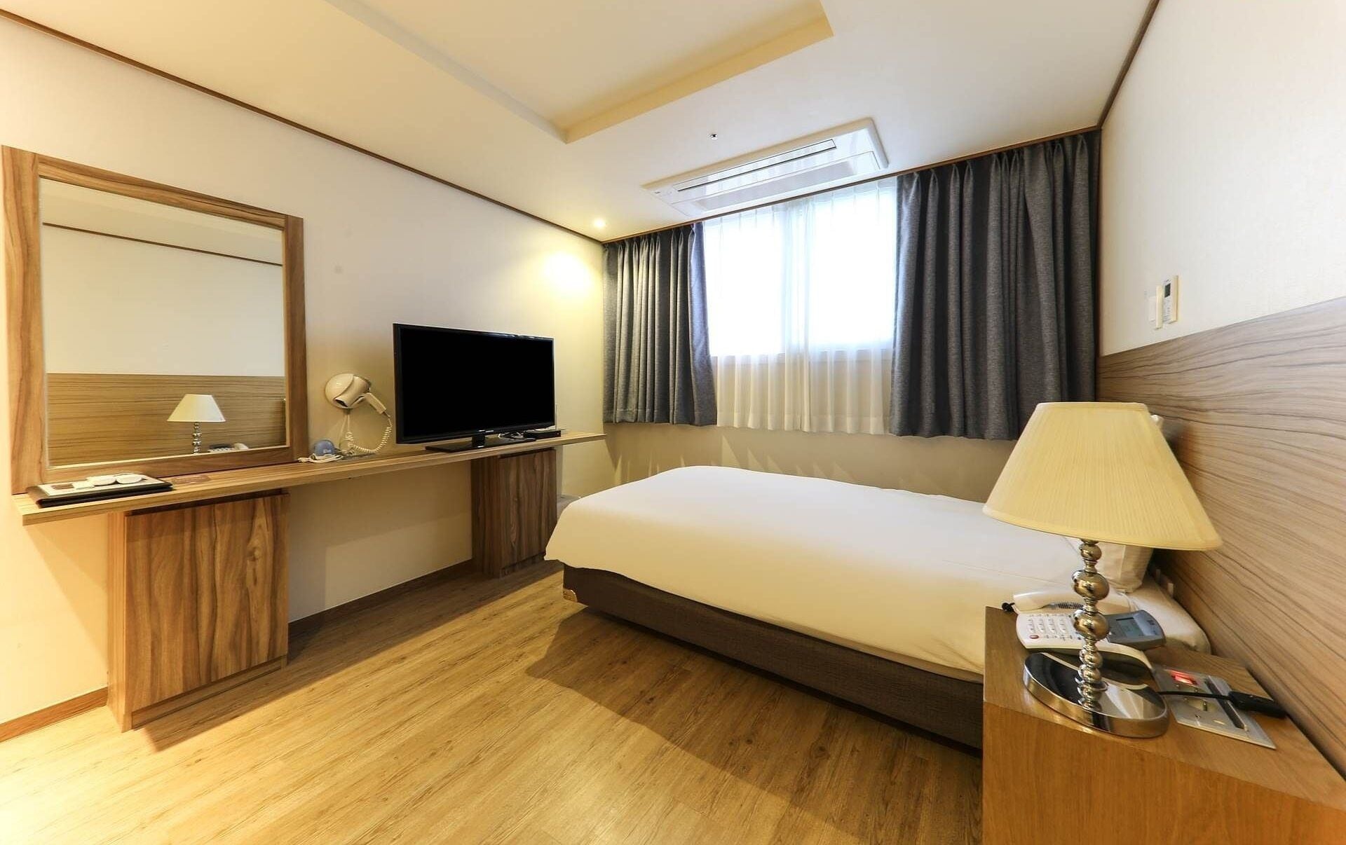 Habitación de hotel con cama, escritorio con televisor, espejo y lámpara.