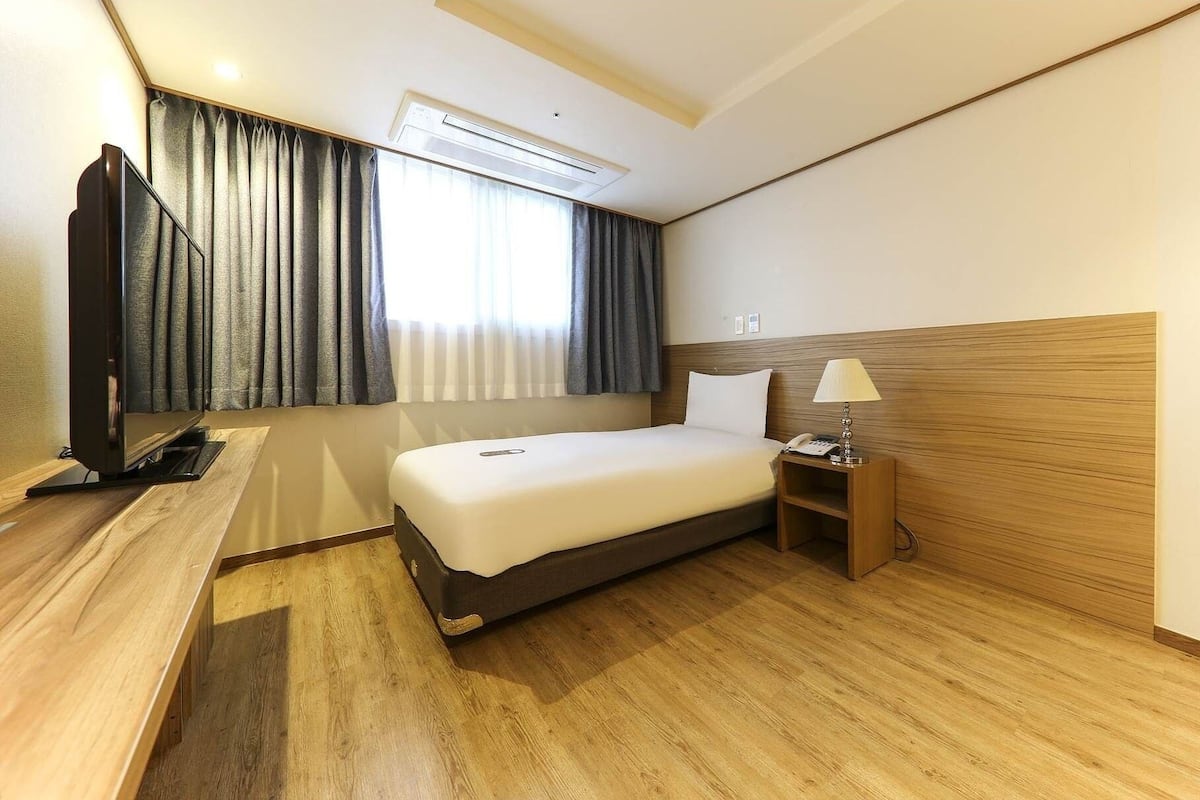 A hotel room with a bed, a desk, a television, a lamp, and an air conditioning unit.