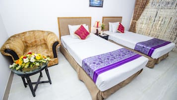 A hotel room with two beds, a sofa, a table with flowers, and a nightstand with a lamp.