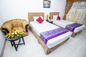 A hotel room with two beds, a sofa, a table with flowers, and a nightstand with a lamp. - Hotel Lake Breeze (Dhaka)