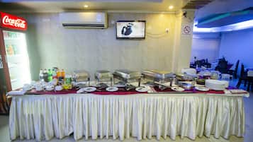 A buffet setup with multiple serving stations, a Coca-Cola refrigerator, and a television mounted on the wall.