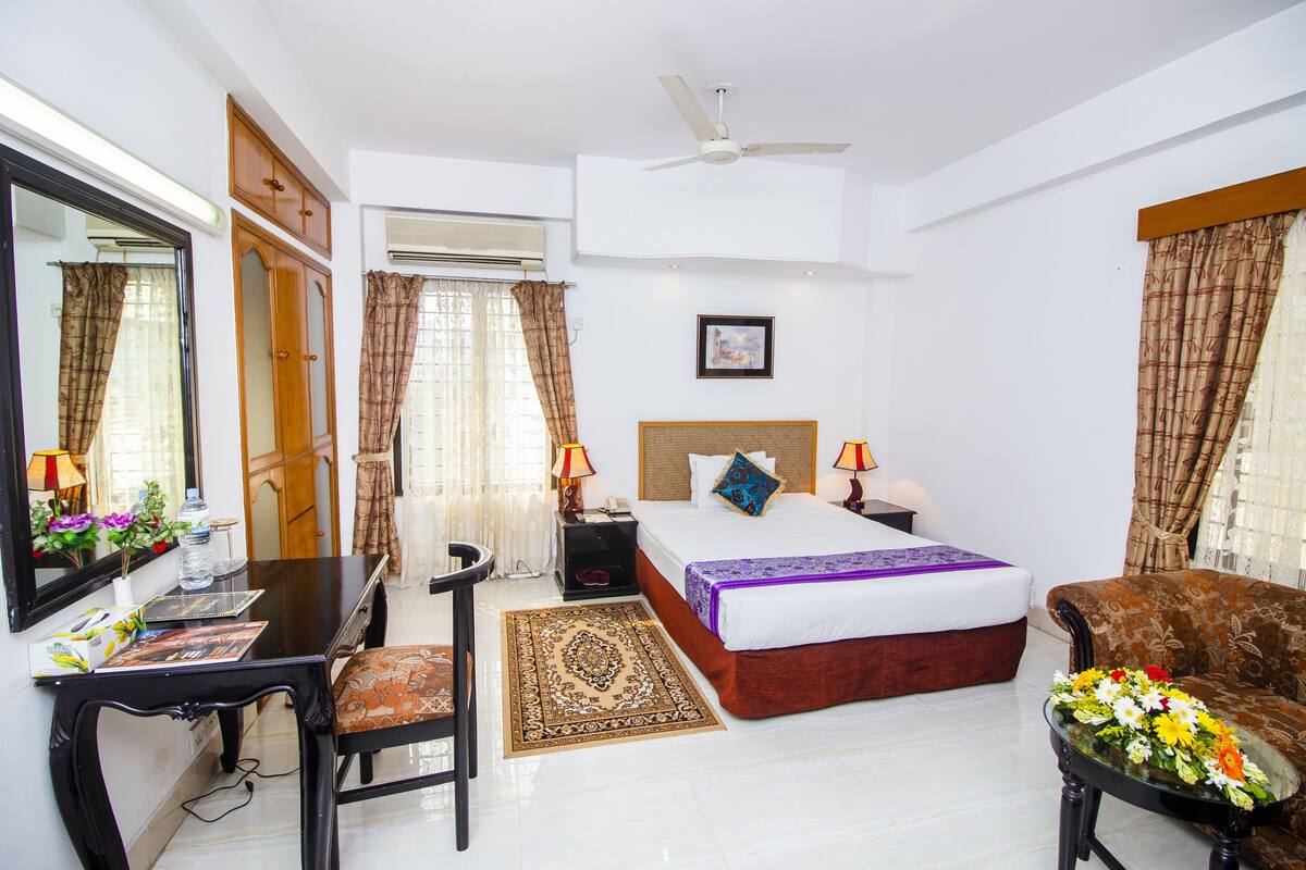 A hotel room with a bed, a desk, a chair, a sofa, and a ceiling fan.