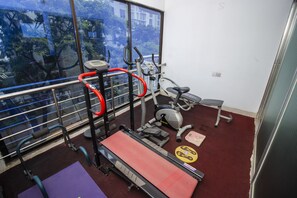 A gym with exercise equipment, a treadmill, and a window with a view of trees. - Hotel Lake Breeze (Dhaka)