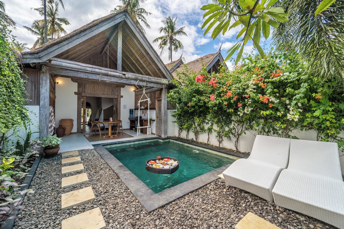 A pool with a floating bar, a white outdoor sofa, and a thatched-roof building.