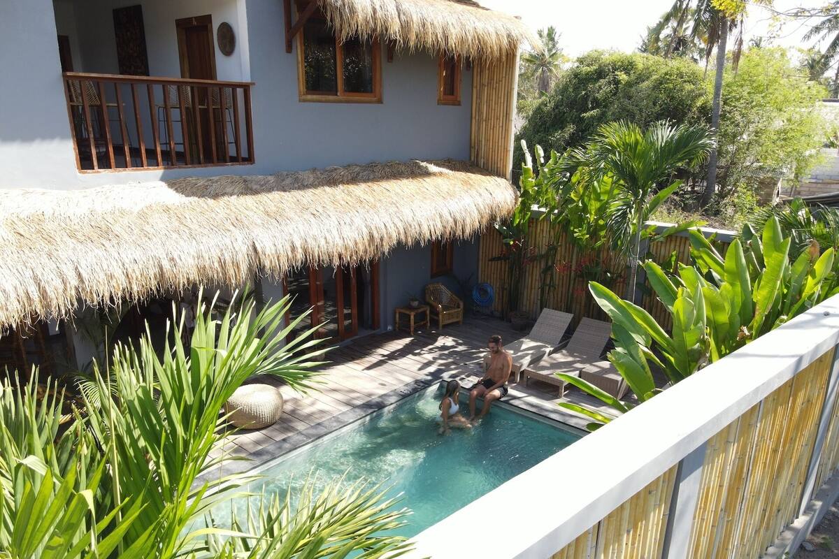 A pool area with lounge chairs and a thatched-roof building.