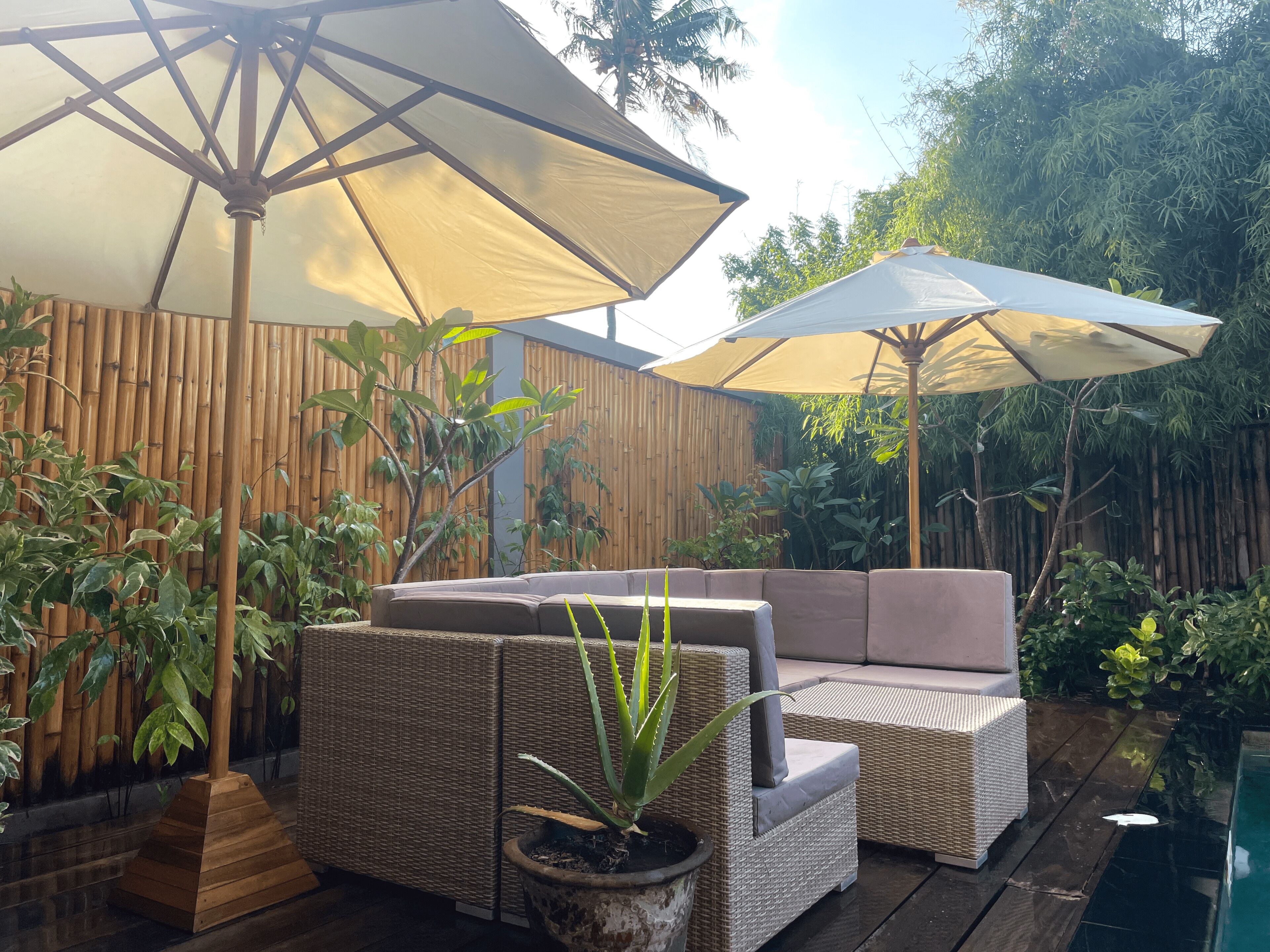 A patio area with wicker furniture and two large umbrellas, surrounded by bamboo fencing and various plants.
