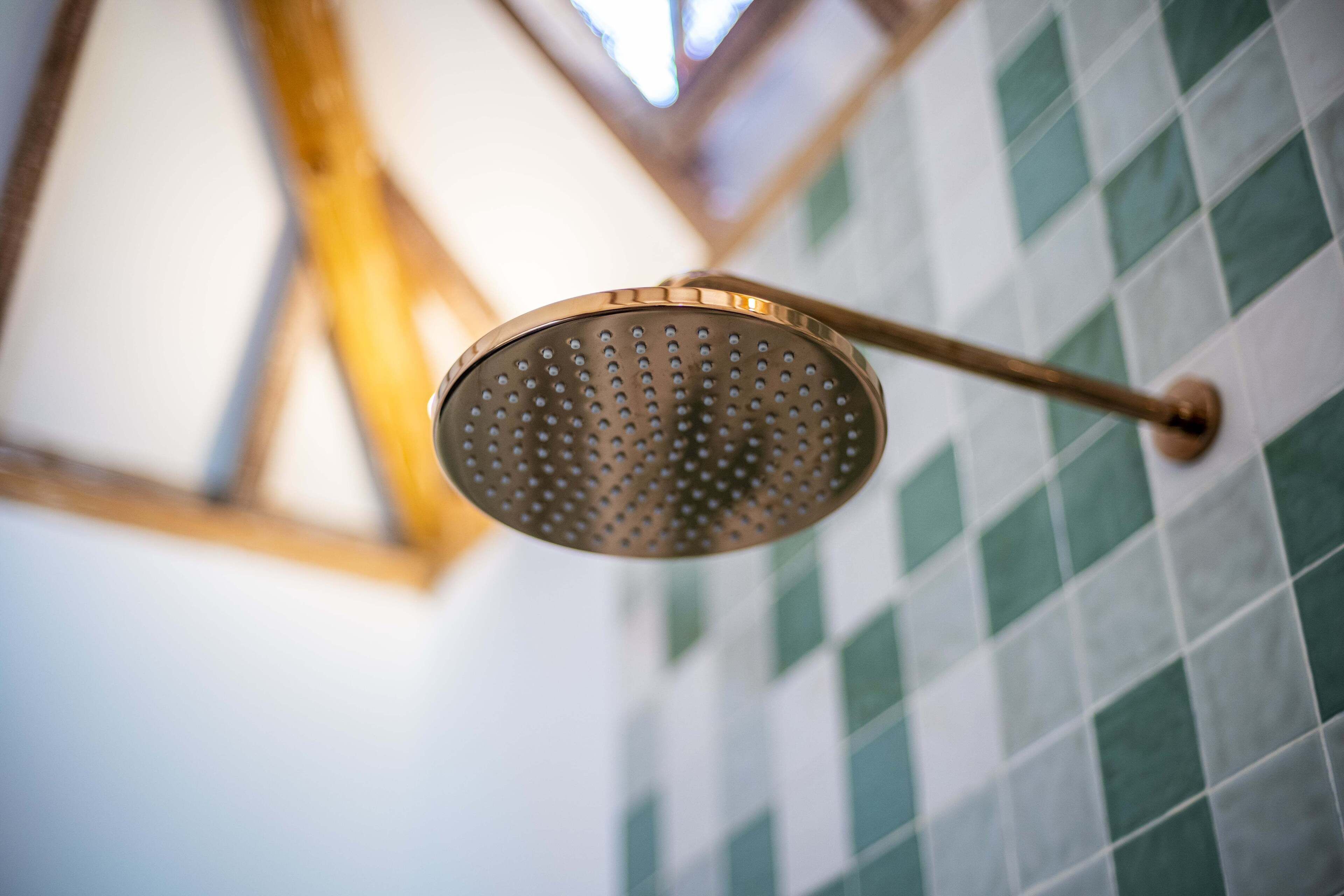 A showerhead with a perforated design, mounted on a wall with a checkered tile pattern.