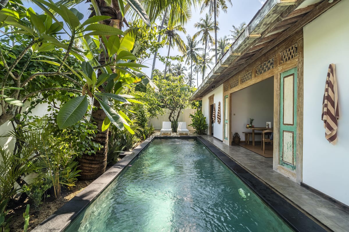 A pool with a tiled edge, surrounded by lush greenery and a building with a traditional design.