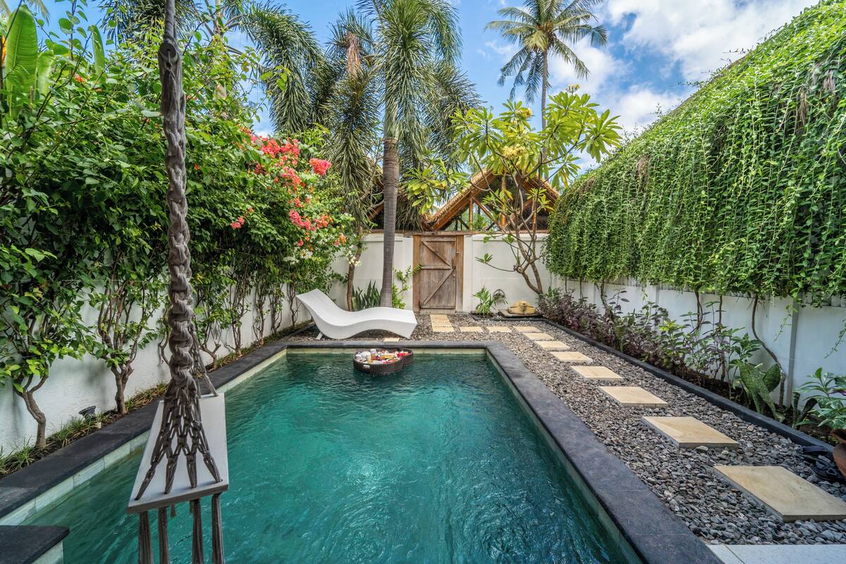 A swimming pool with a white lounge chair, surrounded by lush greenery and palm trees.