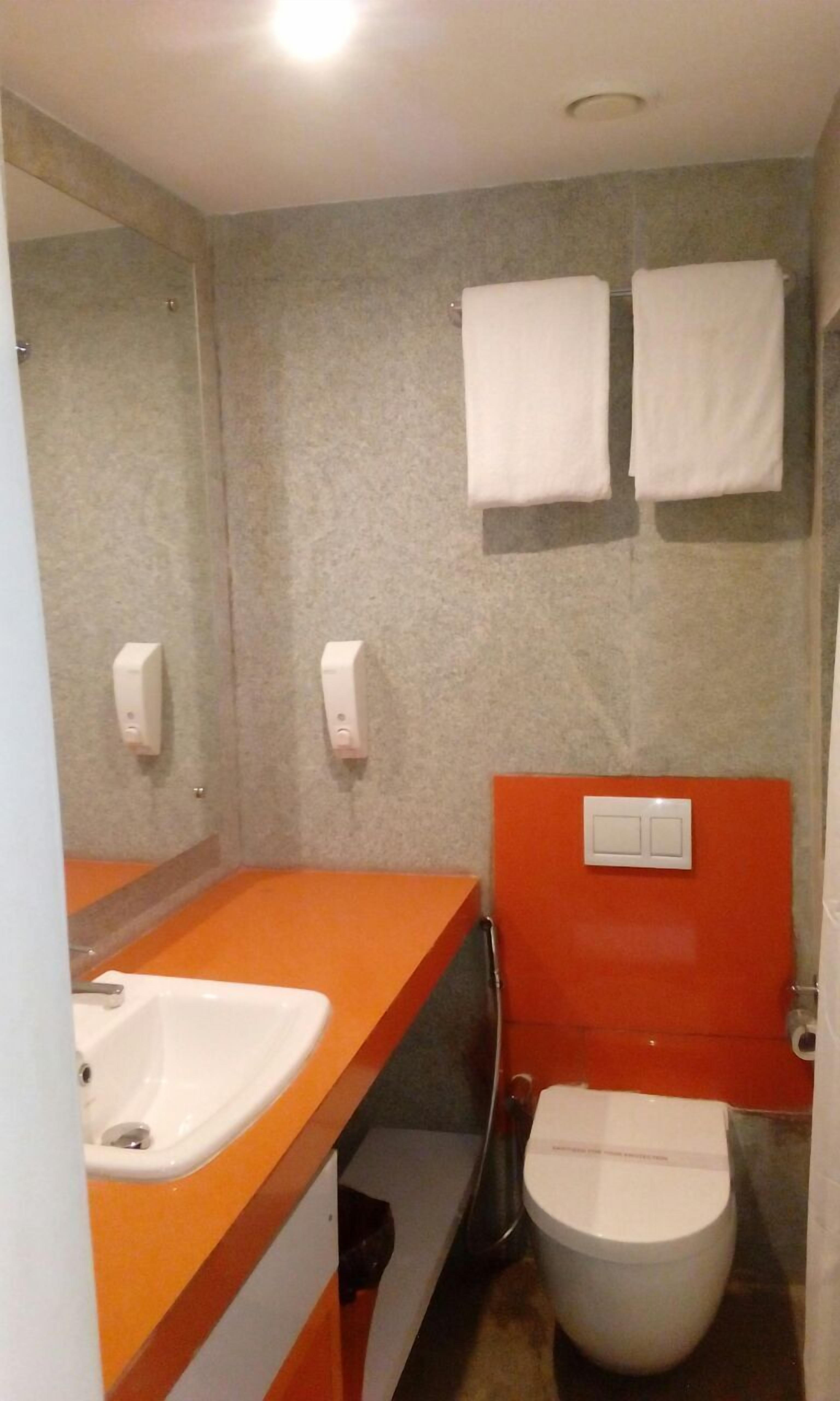 A bathroom with a white sink, a toilet, and two hand dryers on the wall.