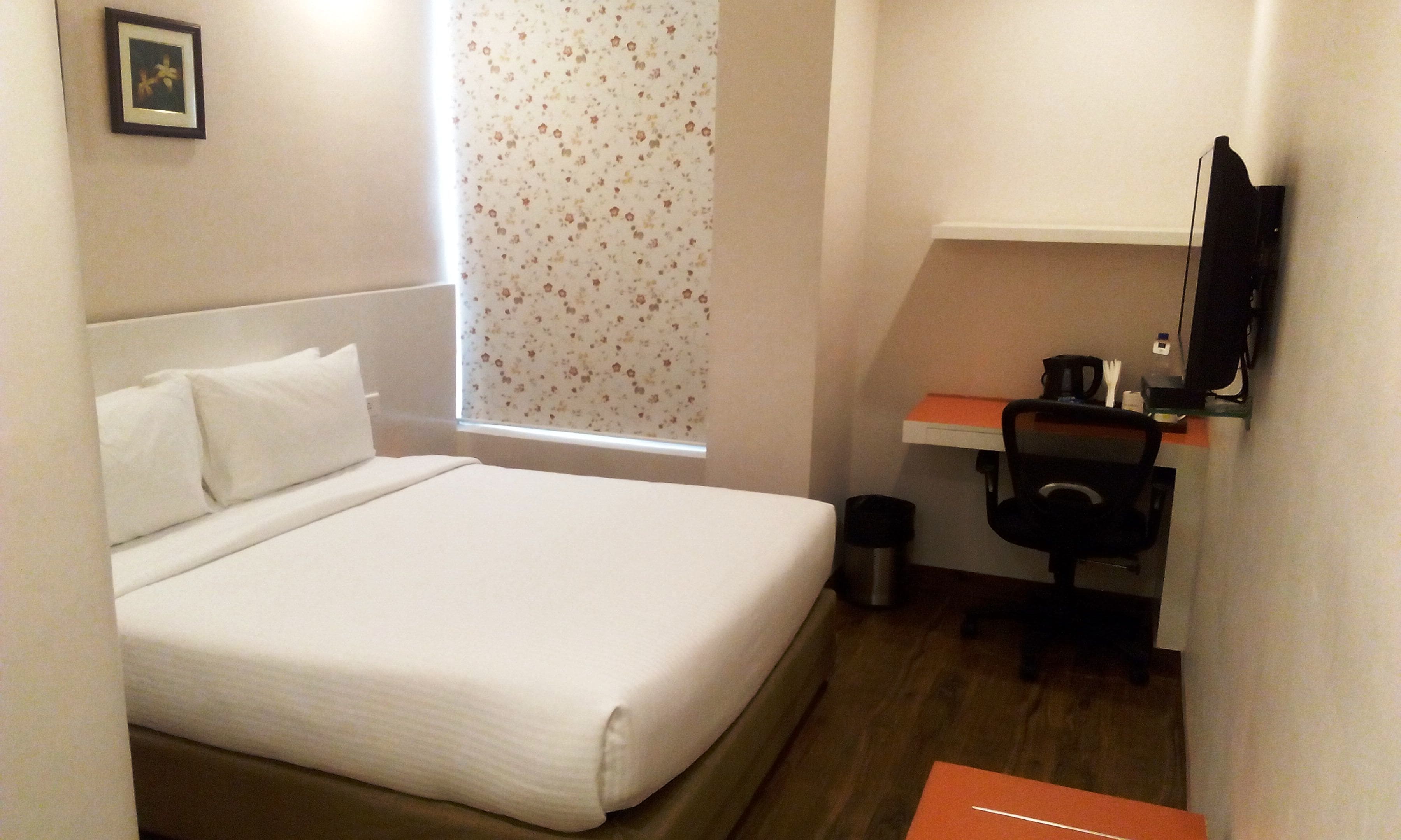 A small hotel room with a single bed, a desk, a chair, and a television.
