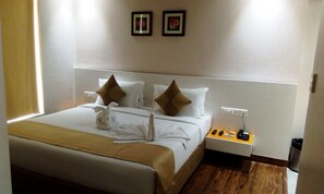 Habitación de hotel con una cama bien hecha, dos almohadas, una mesita de noche con teléfono y controles remotos, y un enchufe en la pared.