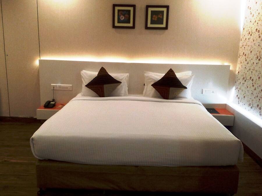 A hotel room with a large bed, two bedside tables, a nightstand with a phone, and a wall-mounted light.
