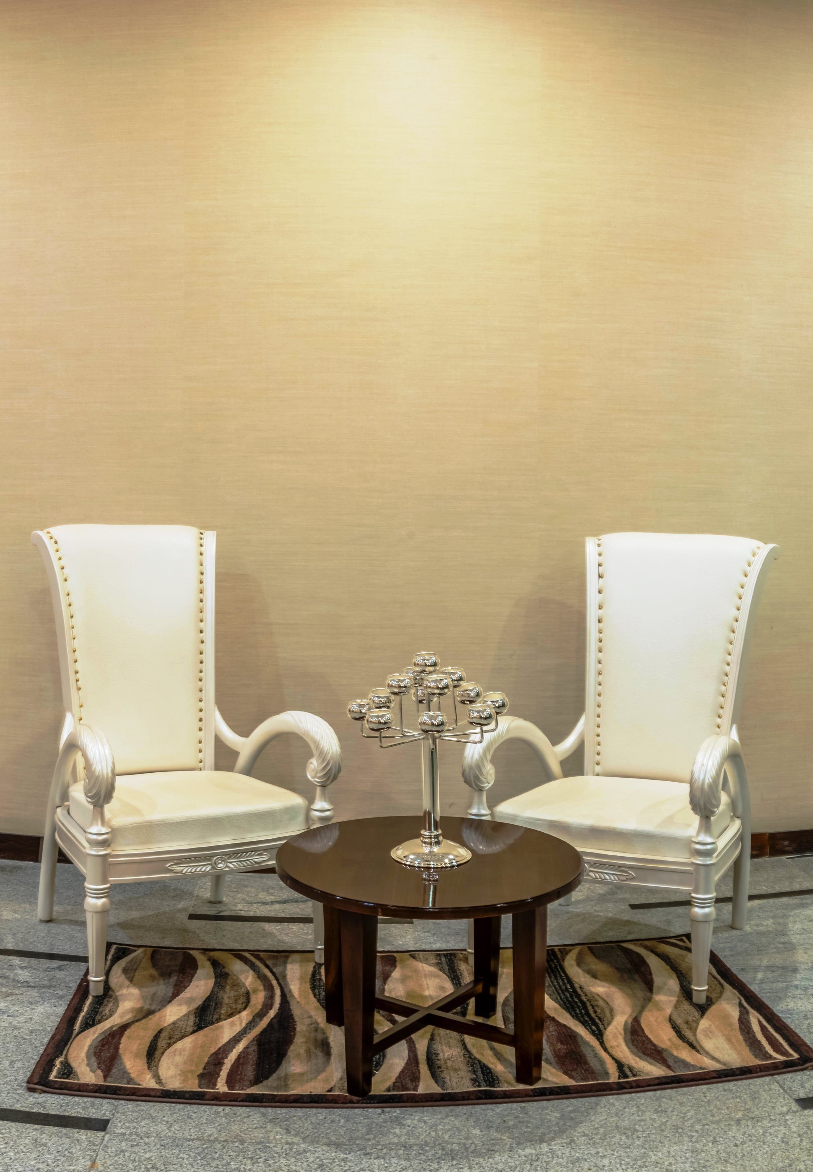 Two white upholstered chairs with gold accents, a small round table with a glass top, and a decorative metal candelabra.