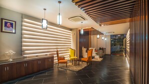 A modern reception area with a dark tiled floor, a wooden reception desk, and a yellow chair. - Mango Hotels Prangan, Bhubaneshwar (Bhubaneshwar)