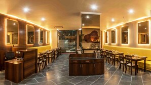 A restaurant with a central bar, multiple dining tables, and a reception desk. - Mango Hotels Prangan, Bhubaneshwar (Bhubaneshwar)