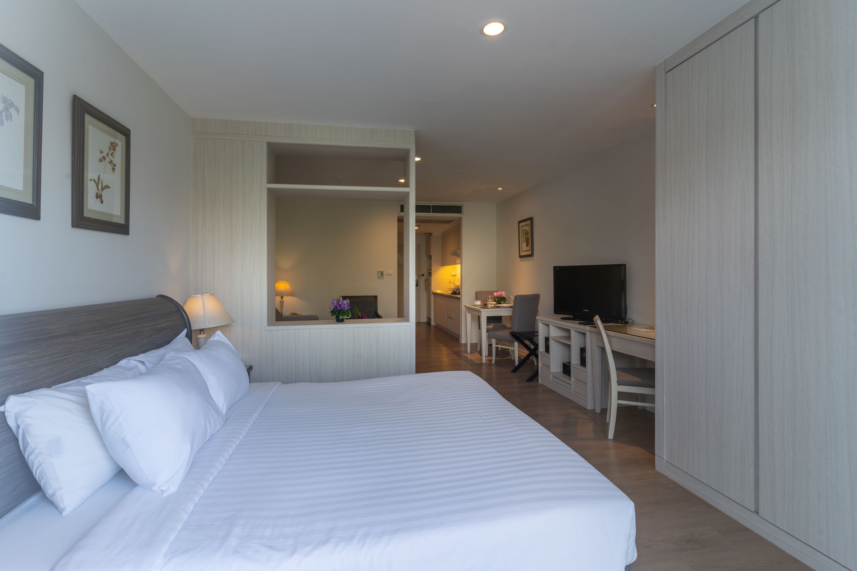 A hotel room with a bed, desk, chair, television, and a wardrobe.